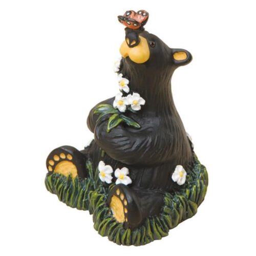 Cute bear figurine sitting on grass with flowers.
