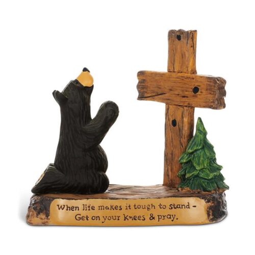 A bear figurine prays beside a cross with an inspirational quote.