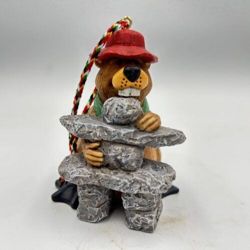 A bear figurine sitting on a stone structure, wearing a red hat.