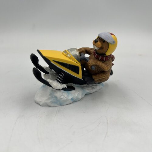 A small figurine of a person riding a yellow snowmobile on a snowy base.