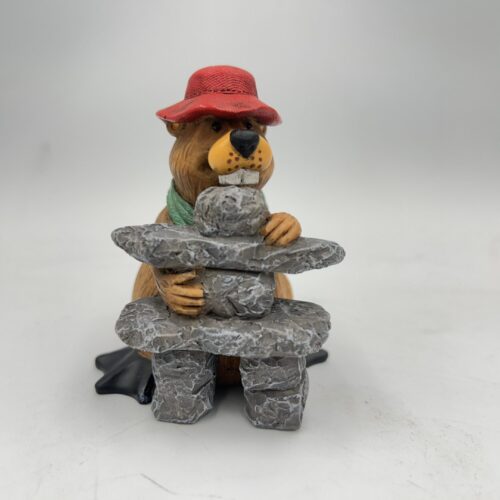 A raccoon figurine wearing a red hat and sunglasses, holding a fish at a stone table.